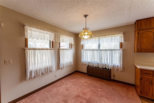 unfurnished dining area with wallpapered walls, baseboards, a textured ceiling, and light colored carpet