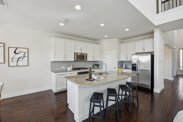 kitchen with visible vents, arched walkways, stainless steel appliances, a kitchen bar, and a sink