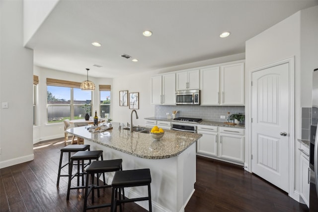 kitchen with a breakfast bar, dark wood finished floors, stainless steel microwave, backsplash, and a sink