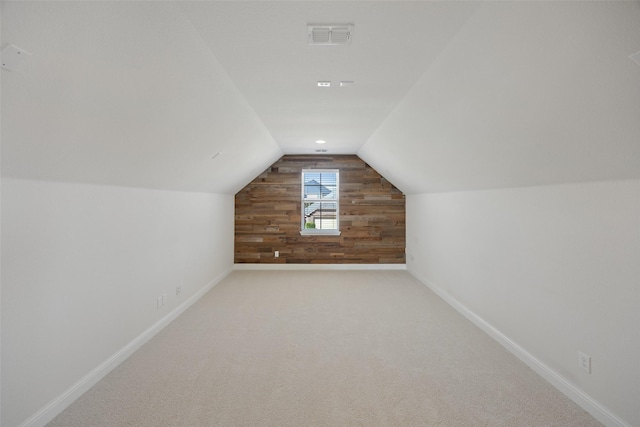 additional living space featuring wood walls, visible vents, baseboards, vaulted ceiling, and carpet