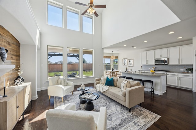 living room with baseboards, a ceiling fan, a towering ceiling, dark wood-style flooring, and recessed lighting