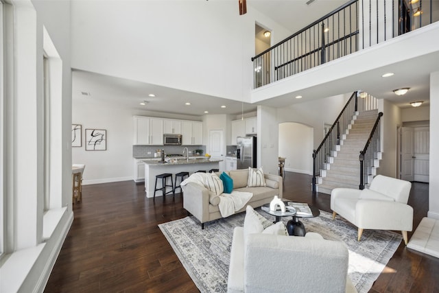 living area with baseboards, stairs, arched walkways, and dark wood-style flooring