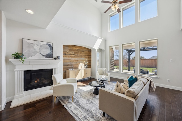 living area with ceiling fan, wood-type flooring, a glass covered fireplace, and baseboards