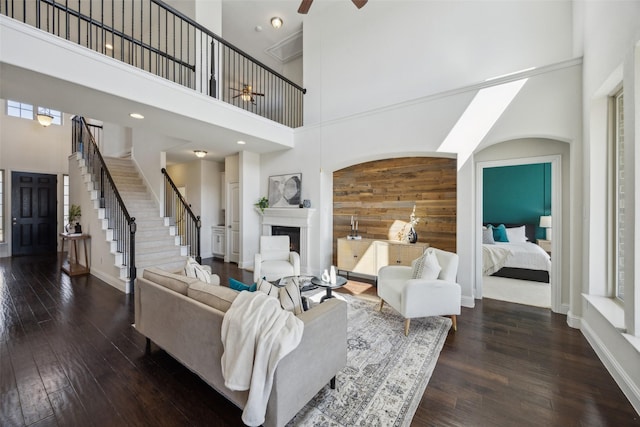 living room with a towering ceiling, a fireplace, stairway, and dark wood-type flooring