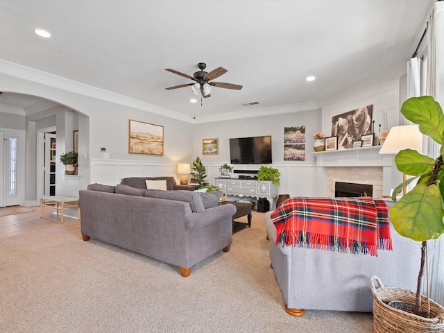 carpeted living area featuring visible vents, a fireplace, arched walkways, and ornamental molding