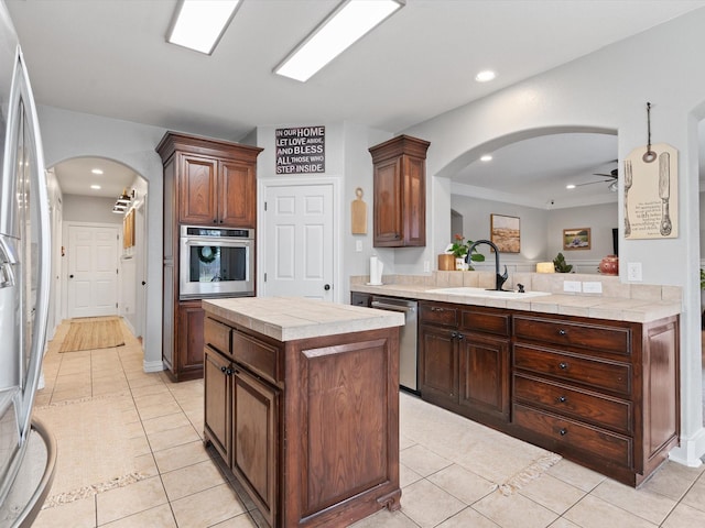 kitchen featuring arched walkways, light tile patterned floors, stainless steel appliances, a sink, and a center island