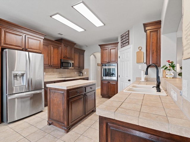 kitchen with arched walkways, light tile patterned floors, stainless steel appliances, a sink, and decorative backsplash