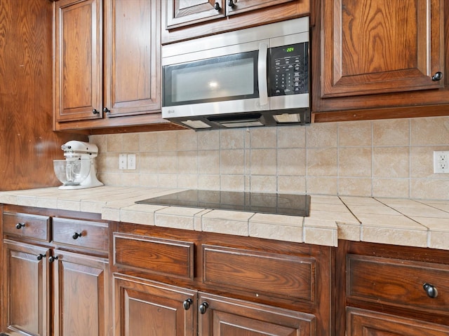 kitchen with tile countertops, black electric stovetop, stainless steel microwave, and decorative backsplash