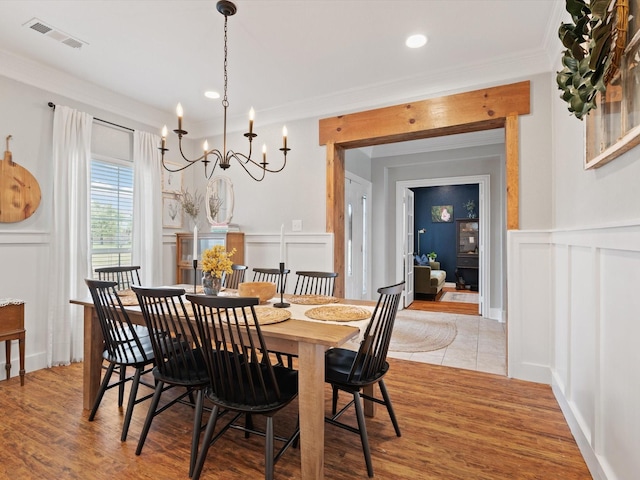 dining space with ornamental molding, light wood-type flooring, visible vents, and a decorative wall