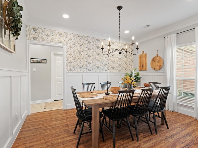 dining area with a wainscoted wall, crown molding, visible vents, and wood finished floors