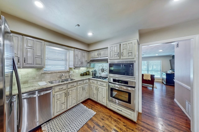 kitchen featuring dark wood-style floors, decorative backsplash, appliances with stainless steel finishes, a sink, and under cabinet range hood