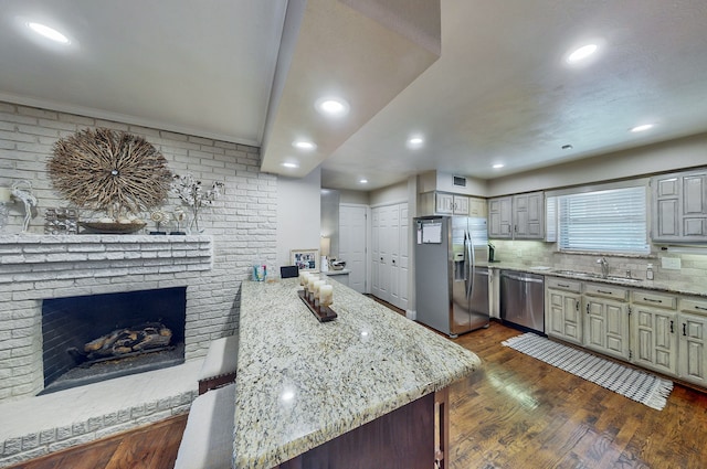 kitchen featuring stainless steel appliances, dark wood-type flooring, a peninsula, backsplash, and light stone countertops