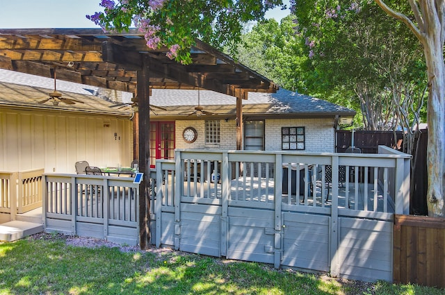 view of front of property with ceiling fan, roof with shingles, fence, a deck, and brick siding