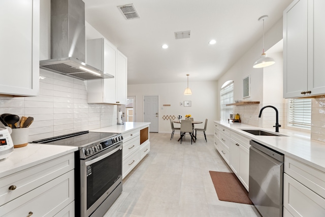 kitchen featuring stainless steel appliances, a sink, visible vents, wall chimney exhaust hood, and decorative light fixtures