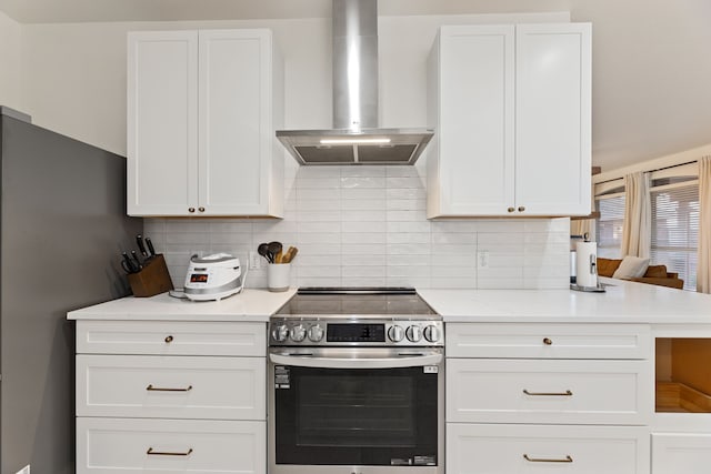 kitchen featuring light stone counters, stainless steel appliances, white cabinetry, decorative backsplash, and wall chimney exhaust hood