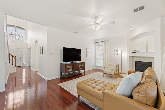 living area featuring a tile fireplace, ceiling fan with notable chandelier, wood finished floors, visible vents, and baseboards