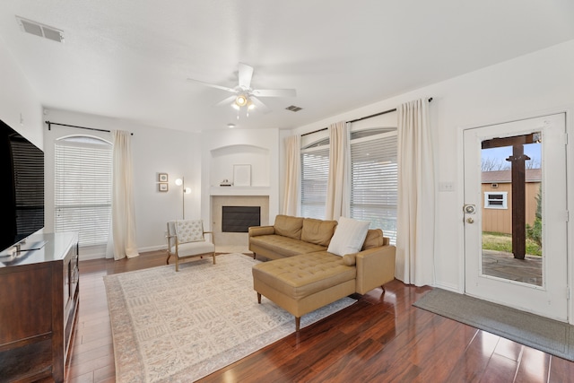 living room featuring dark wood-style floors, a wealth of natural light, a fireplace, and visible vents