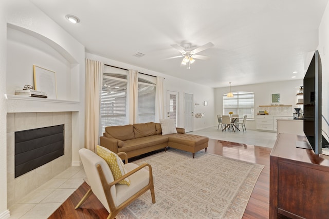 living room featuring light wood-style flooring, visible vents, a ceiling fan, and a tiled fireplace