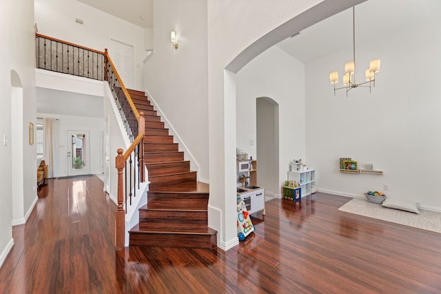 entryway with stairway, arched walkways, a towering ceiling, and wood finished floors