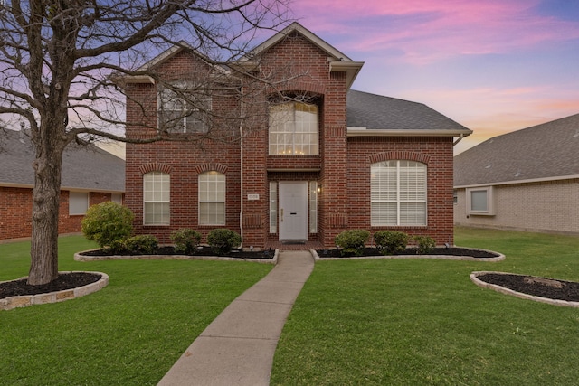 traditional home featuring brick siding, a lawn, and a shingled roof