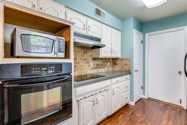 kitchen with under cabinet range hood, white cabinetry, black appliances, tasteful backsplash, and dark countertops