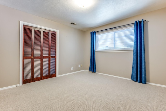 empty room with carpet floors, visible vents, a textured ceiling, and baseboards