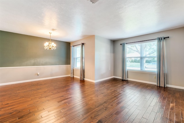 spare room with dark wood-type flooring, a healthy amount of sunlight, a notable chandelier, and baseboards