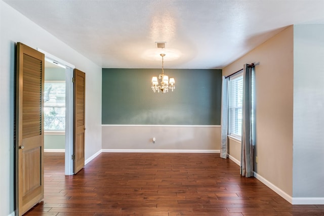 empty room featuring dark wood-style floors, a chandelier, and baseboards