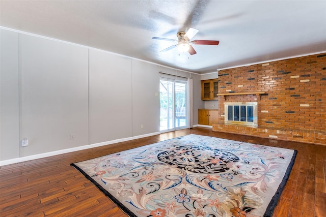 living room with a fireplace, hardwood / wood-style floors, a ceiling fan, brick wall, and baseboards