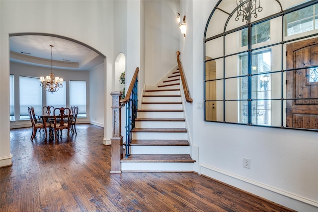 stairway with baseboards, arched walkways, a raised ceiling, wood finished floors, and a notable chandelier