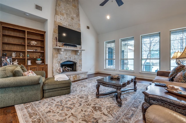 living area featuring visible vents, plenty of natural light, a stone fireplace, and wood finished floors