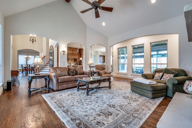 living room featuring arched walkways, high vaulted ceiling, dark wood-type flooring, and ceiling fan with notable chandelier