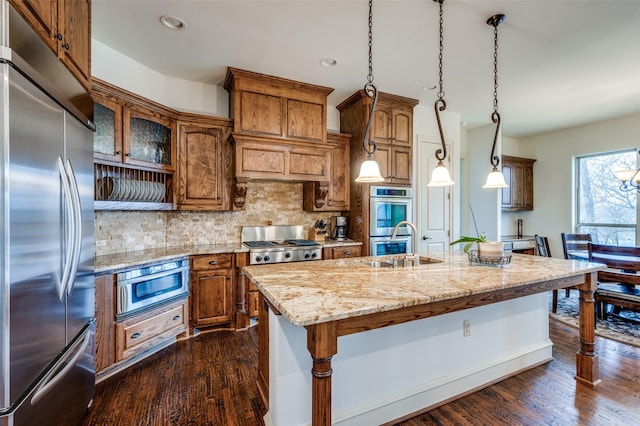 kitchen with dark wood-style floors, decorative backsplash, brown cabinetry, a sink, and built in appliances