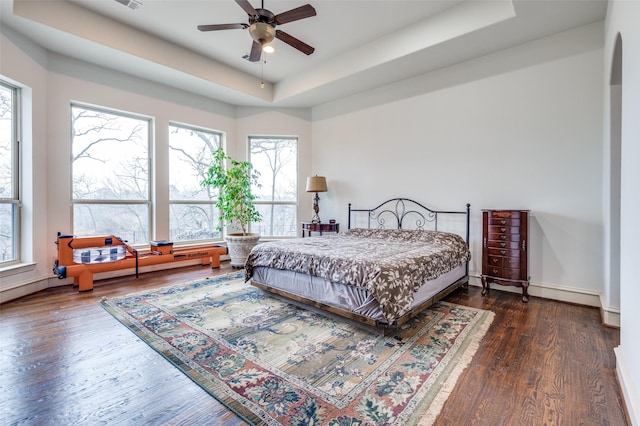 bedroom featuring a raised ceiling, visible vents, baseboards, and wood finished floors