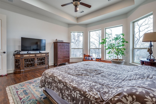 bedroom with baseboards, a tray ceiling, visible vents, and wood finished floors