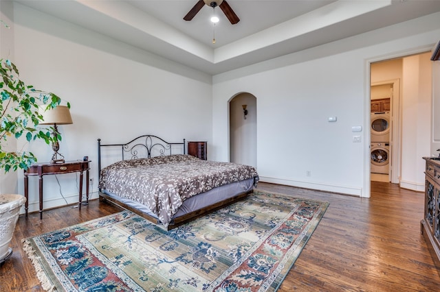 bedroom featuring arched walkways, stacked washing maching and dryer, wood finished floors, and baseboards