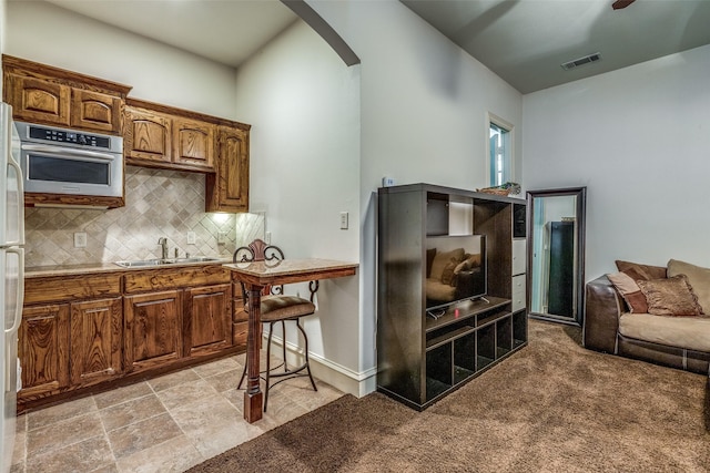 kitchen with arched walkways, a sink, visible vents, stainless steel oven, and decorative backsplash