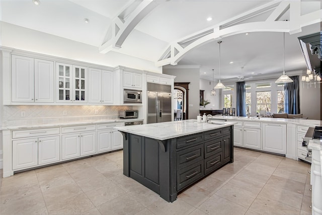 kitchen with built in appliances, tasteful backsplash, a center island with sink, and white cabinetry