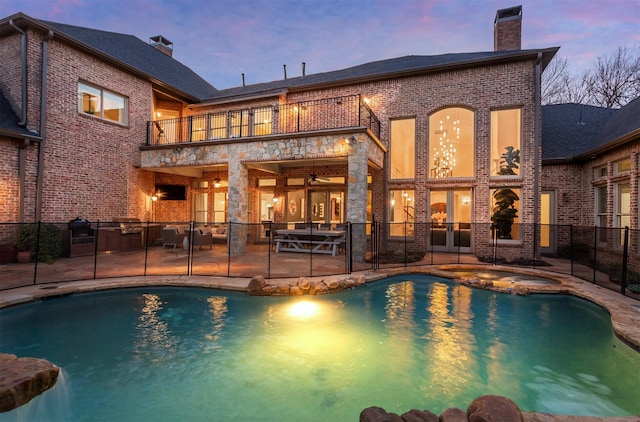 pool at dusk with fence, a pool with connected hot tub, a ceiling fan, and a patio area