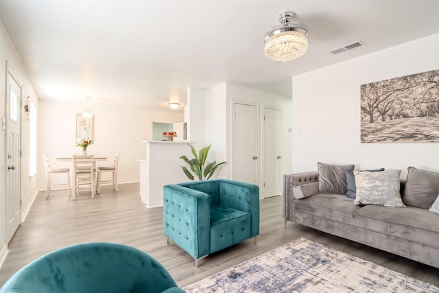 living room featuring baseboards, wood finished floors, visible vents, and an inviting chandelier