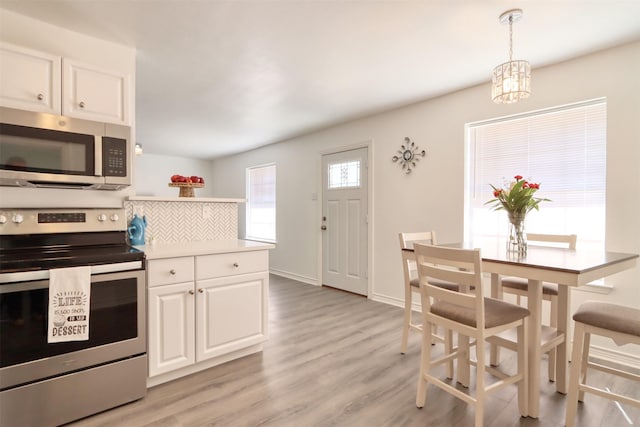 kitchen featuring stainless steel appliances, light wood-style floors, white cabinets, light countertops, and decorative backsplash