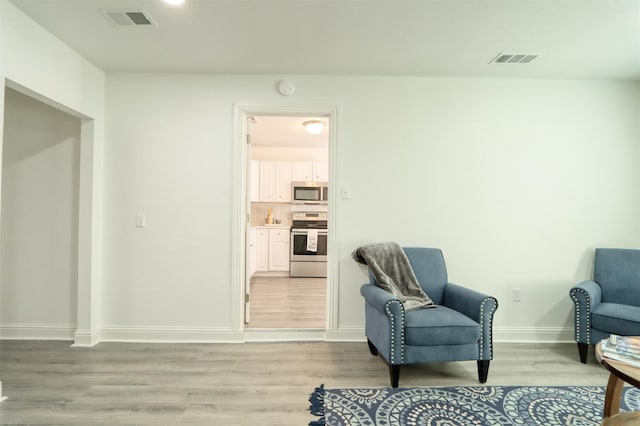 sitting room with light wood-type flooring, visible vents, and baseboards