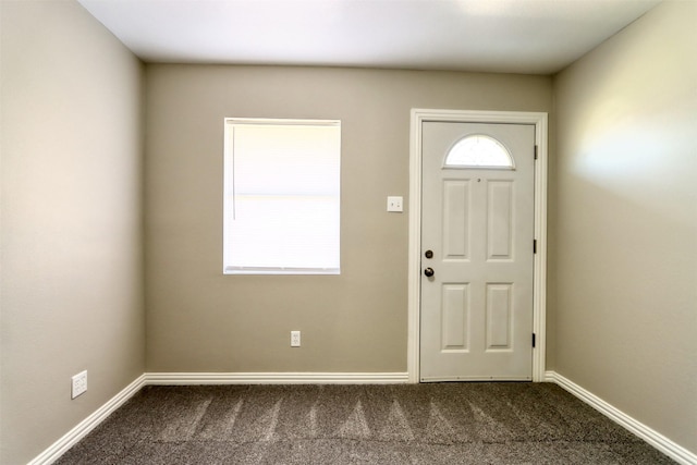 foyer featuring dark carpet and baseboards