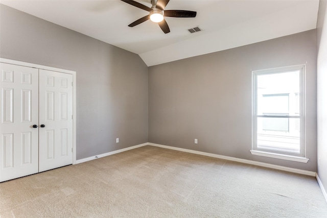 empty room featuring lofted ceiling, baseboards, visible vents, and light colored carpet