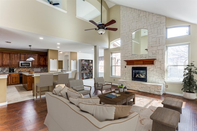 living room featuring plenty of natural light, baseboards, wood finished floors, and a stone fireplace