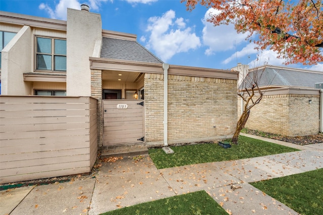 view of side of home featuring a fenced front yard, a gate, a shingled roof, and a chimney