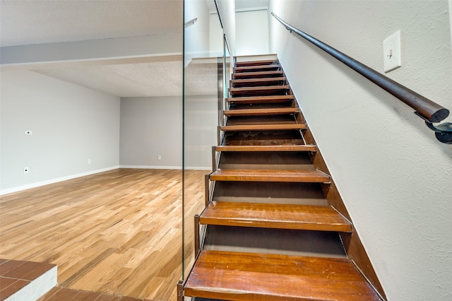 stairs featuring a textured ceiling, wood finished floors, and baseboards