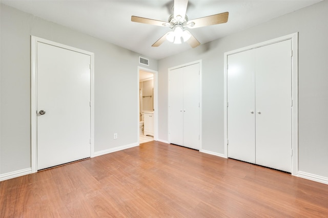 unfurnished bedroom featuring baseboards, wood finished floors, visible vents, and multiple closets