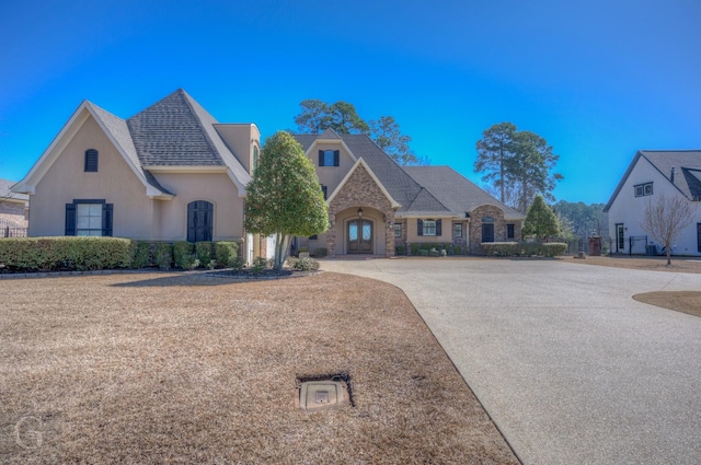 french country style house featuring stone siding, driveway, and stucco siding