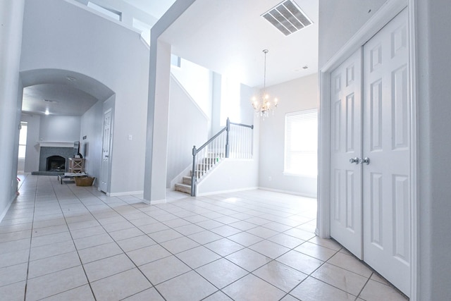 entrance foyer with light tile patterned floors, visible vents, a fireplace with raised hearth, baseboards, and stairs